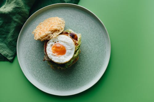 Free Delicious ramen burger topped with a fried egg on a green ceramic plate. Perfect for food photography. Stock Photo