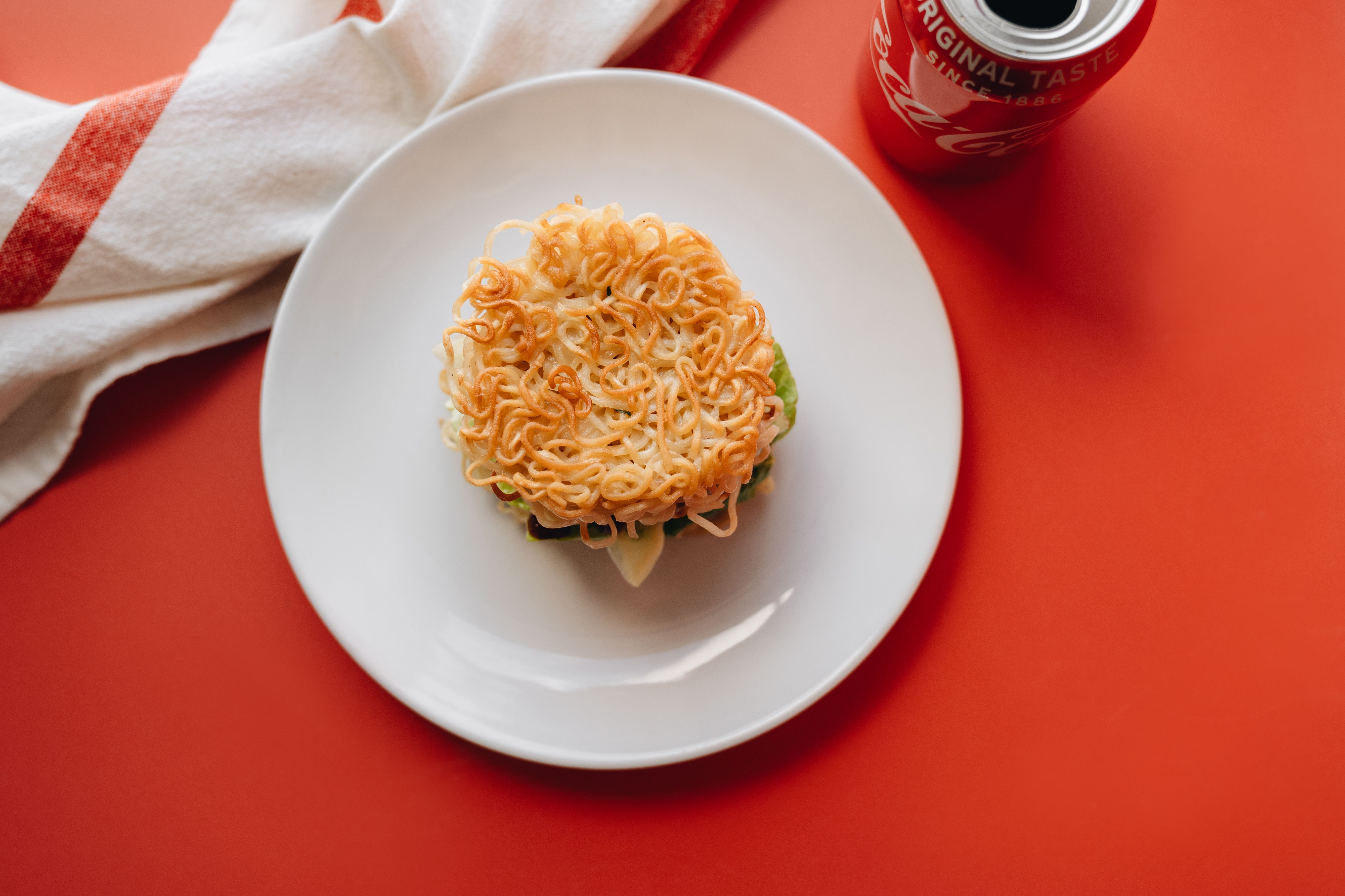 Delicious ramen burger placed on a white plate with a red backdrop, offering a unique culinary twist.