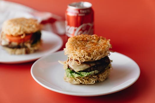 Delicious ramen burger on white plate with soda on a vibrant red background.