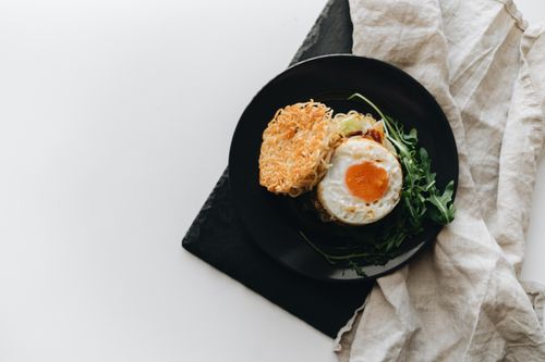 Free Top view of a gourmet ramen noodle dish with fried egg and arugula on a black plate. Stock Photo