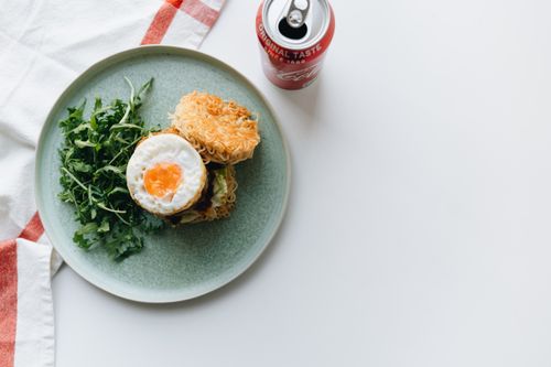 Free Gourmet ramen burger topped with egg and greens alongside a refreshing soda can. Stock Photo