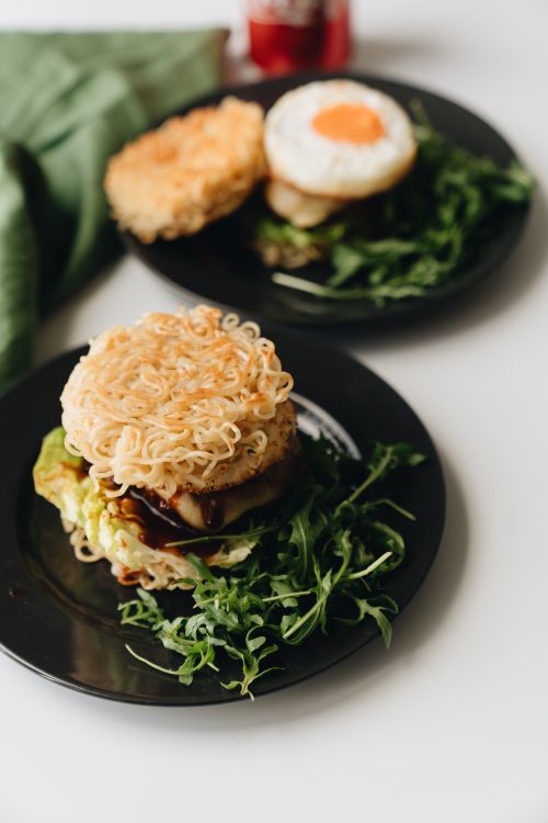 Free Delicious ramen burgers with fried egg and greens, presented on black plates. Perfect for a unique meal. Stock Photo