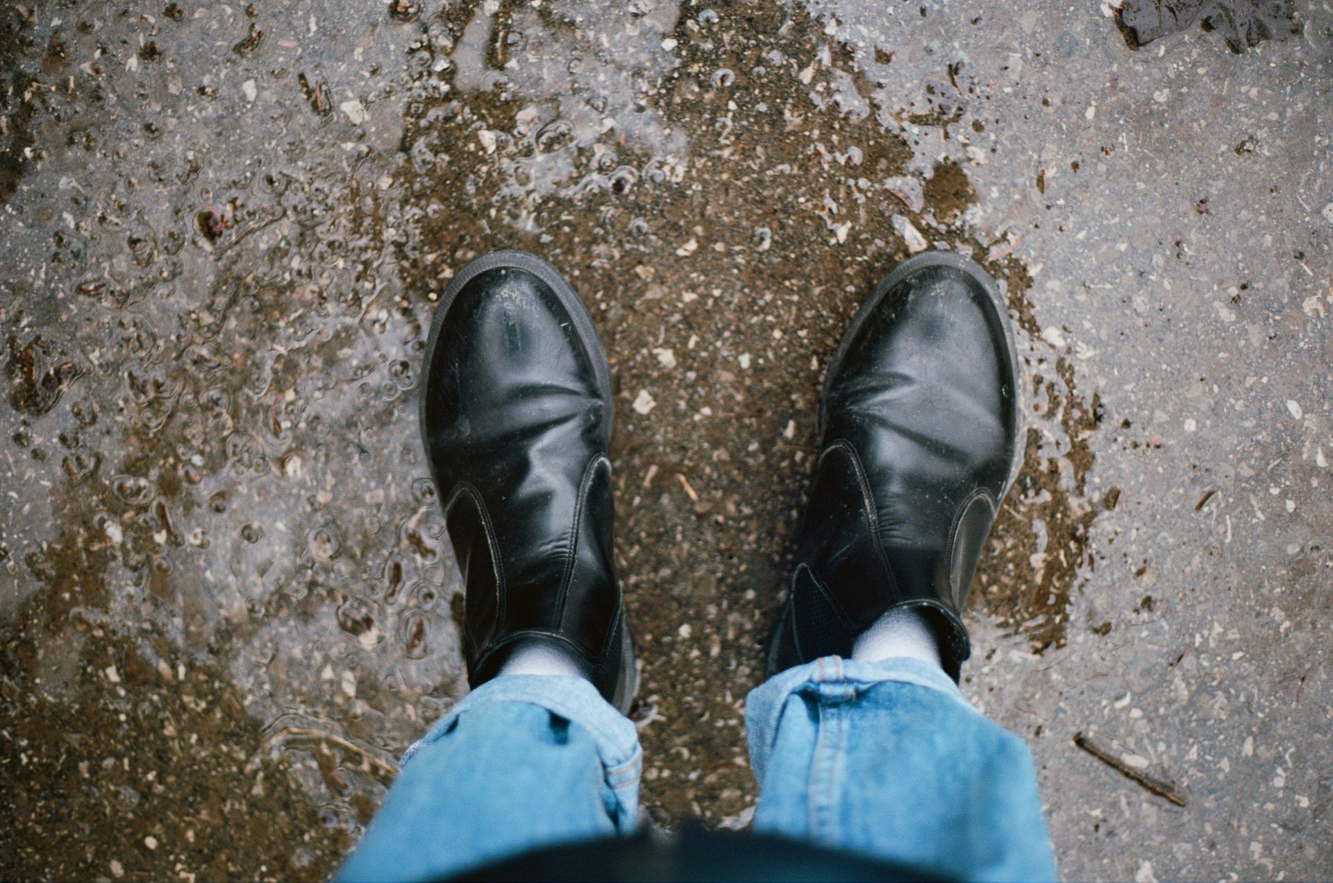 High-angle view of black leather shoes on a wet pavement.