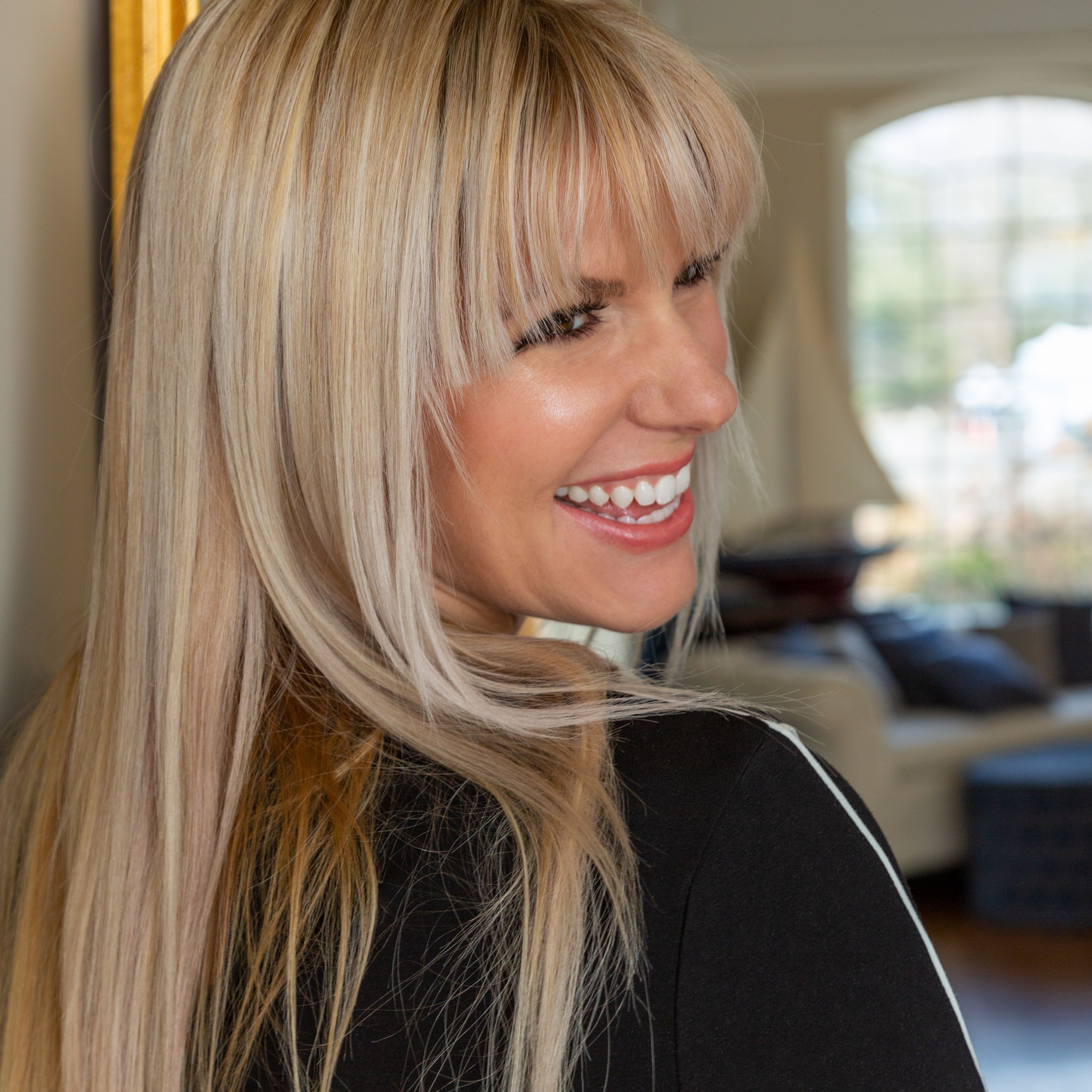 Side view of happy female with blond hair standing in doorway of modern apartment with furniture and window on blurred background