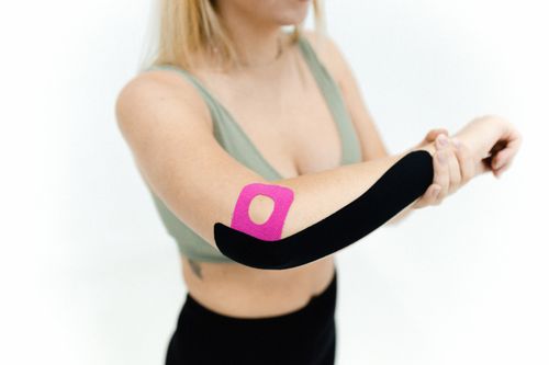 Free Close-up of a woman applying kinesio tape on her arm for therapeutic treatment on a white background. Stock Photo