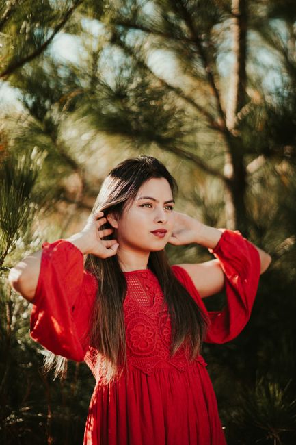 Young female with long hair looking away and touching neck on blurred background of coniferous tree