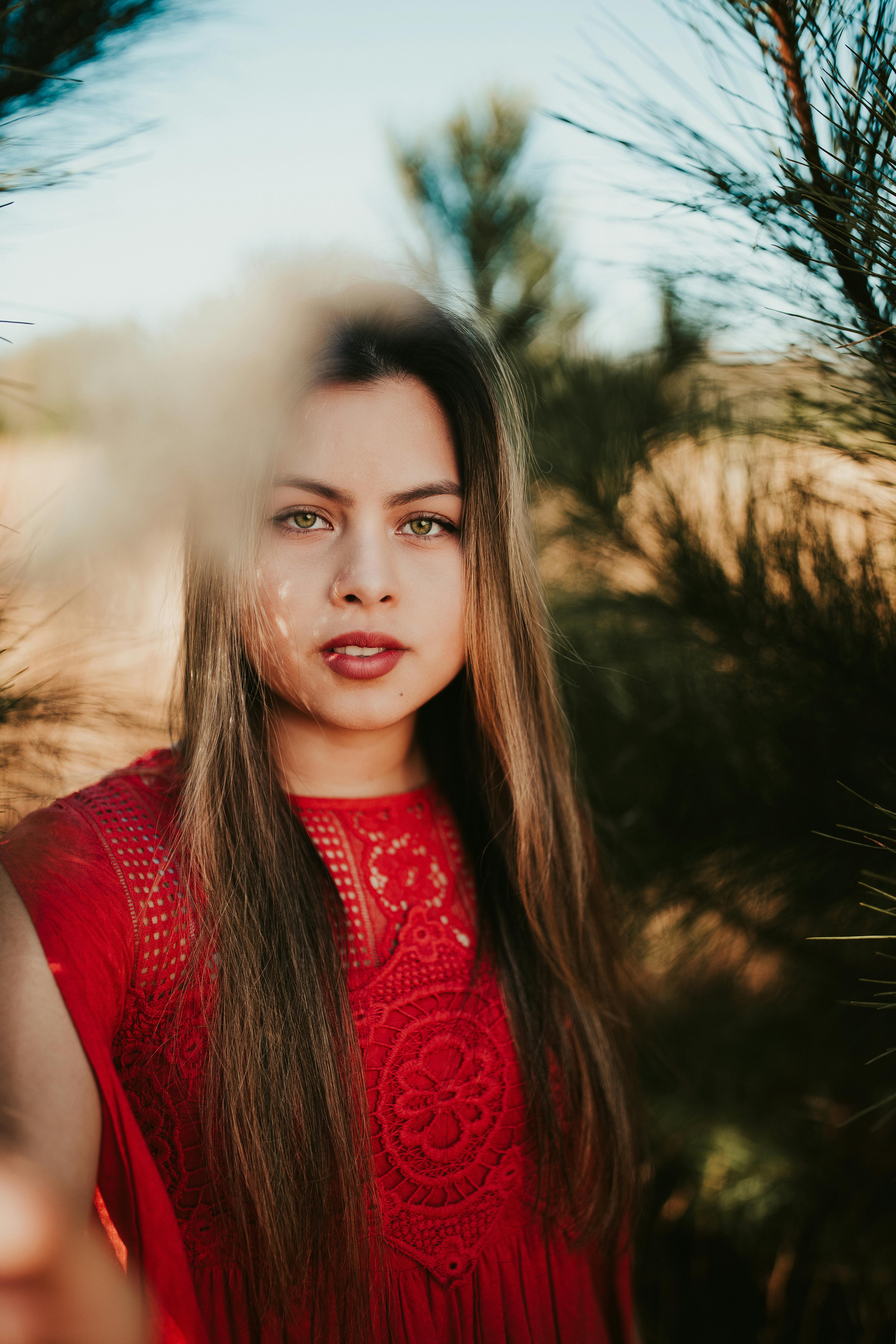 Young content female looking at camera on blurred background of coniferous trees with green needles in daytime