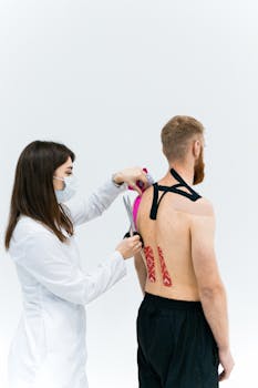A therapist applies kinesiology tape to a man's upper back for muscle support.
