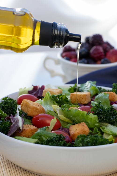 A Person Pouring an Olive Oil on Fresh Salad