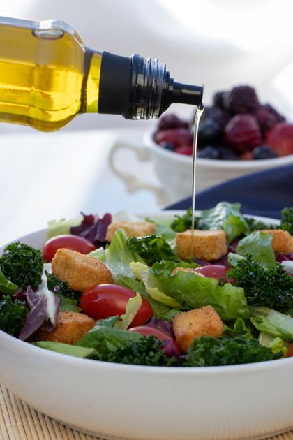 Pessoa despejando azeite de oliva extra virgem sobre salada fresca com tomates e folhas verdes