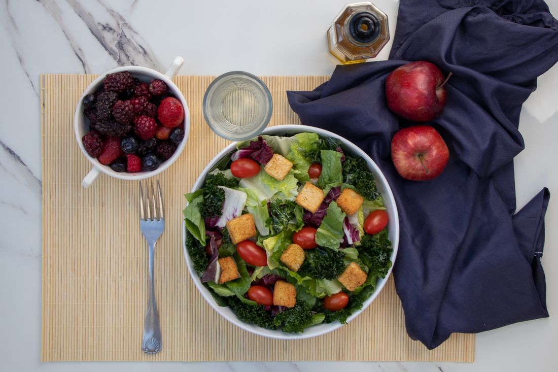 Kale and romaine salad with croutons and cherry tomatoes beside berries and red apples