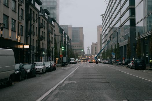 Various vehicles parked on asphalt road between aged and modern buildings against overcast sky in Brussels
