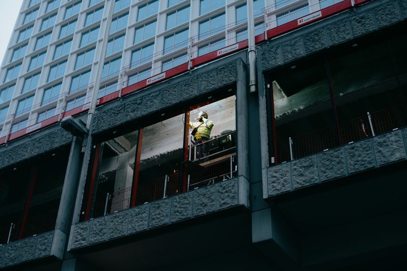 Worker in safety gear near scaffolding at a high-rise facade with glass windows