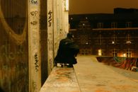 Back view of unrecognizable person in casual outfit and hat riding skateboard on ramp near graffiti wall in city at night