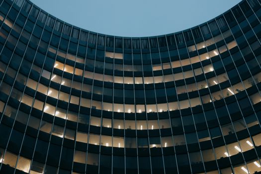 Low angle of modern multistage house facade with shiny lamps under blue sky in town