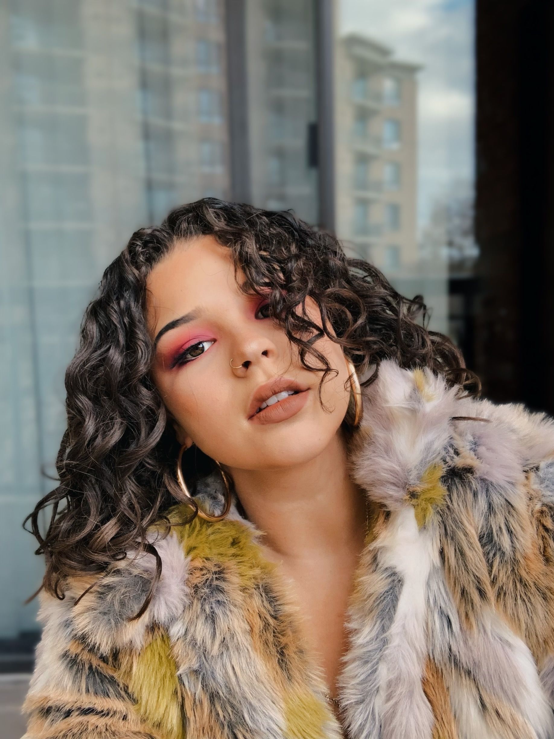 Portrait of a fashionable woman with curly hair and bold makeup wearing a fur coat.