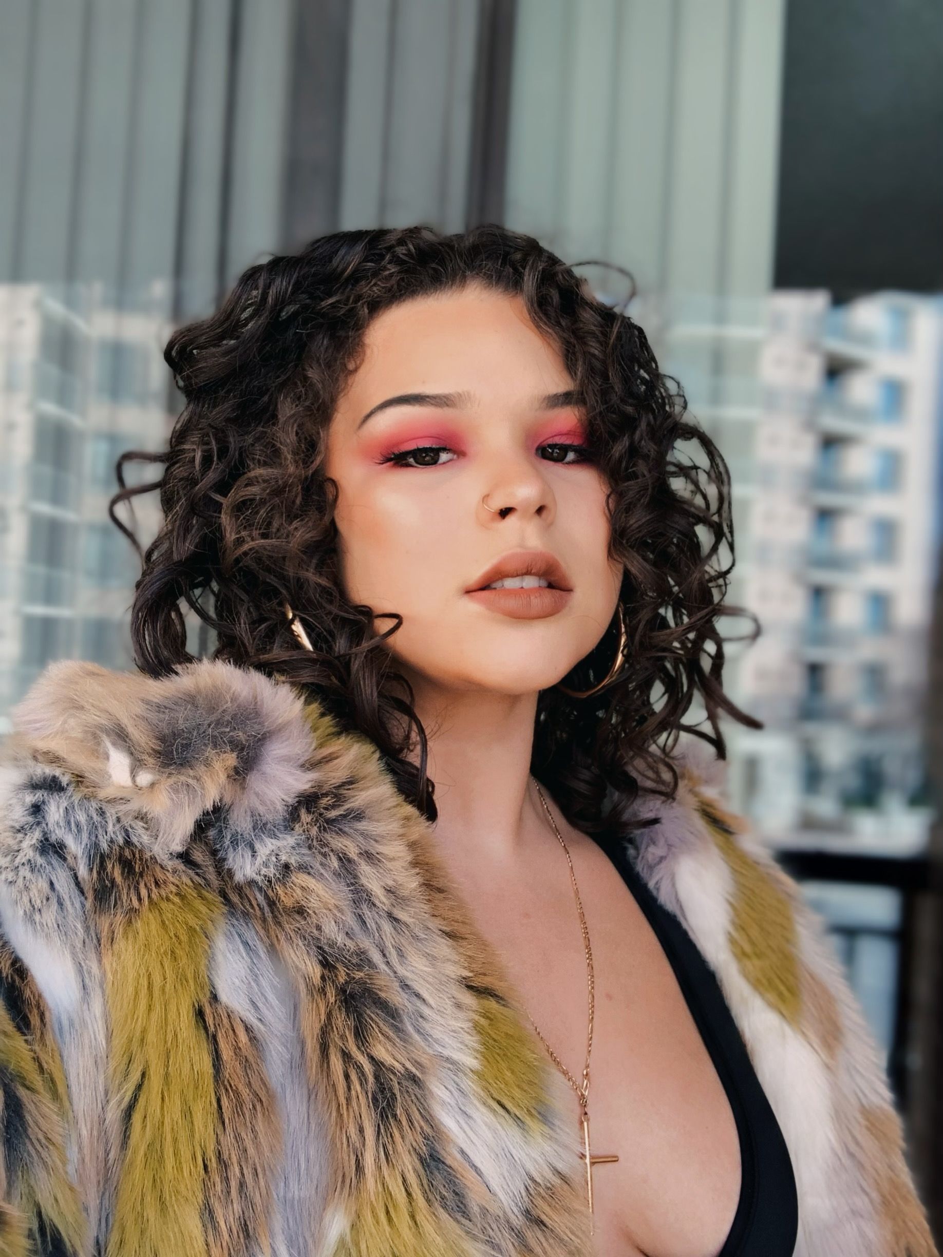 Young woman with bold pink eye makeup and curly hair wearing a fur coat.