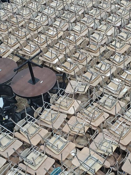 Free Aerial view of neatly stacked metal and wood chairs with round tables in an indoor setting. Stock Photo