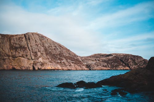 Scenic view of rough brown mounts and wavy blue sea under cloudy sky in daylight