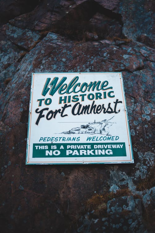 Rectangular shaped vintage signboard with Fort Amherst title and illustration on rugged surface with lichen
