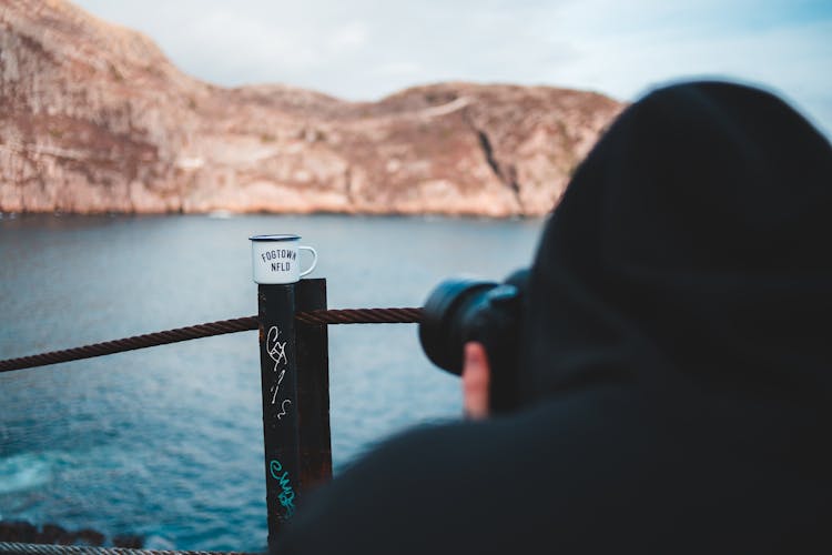 Crop Photographer Taking Photo Of Mug And Ridge On Camera