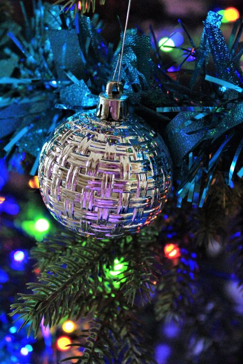 Free Close-up of a silver ornament on a Christmas tree adorned with colorful lights, evoking holiday spirit. Stock Photo
