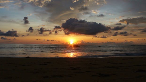 Stunning sunset over the ocean with dramatic clouds and a serene beach view.