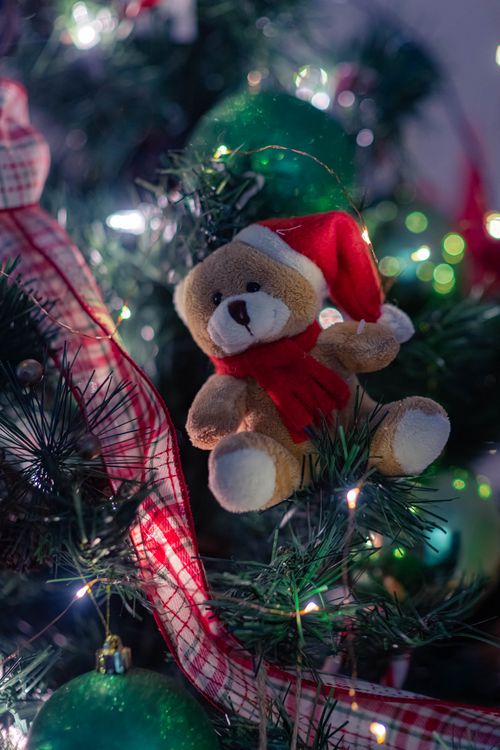 Free Christmas tree close-up featuring a plush teddy bear ornament with festive lights. Stock Photo