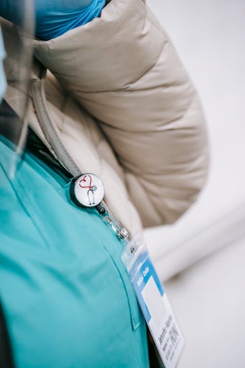 Unrecognizable woman wearing medical uniform and coat with badge on breast attached with round sign with heart and stethoscope