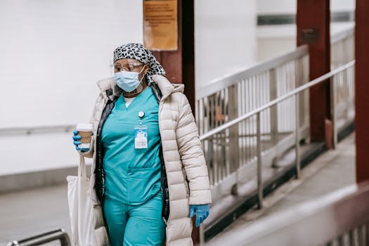 A healthcare professional in a subway wearing a mask and gloves, holding a coffee cup.