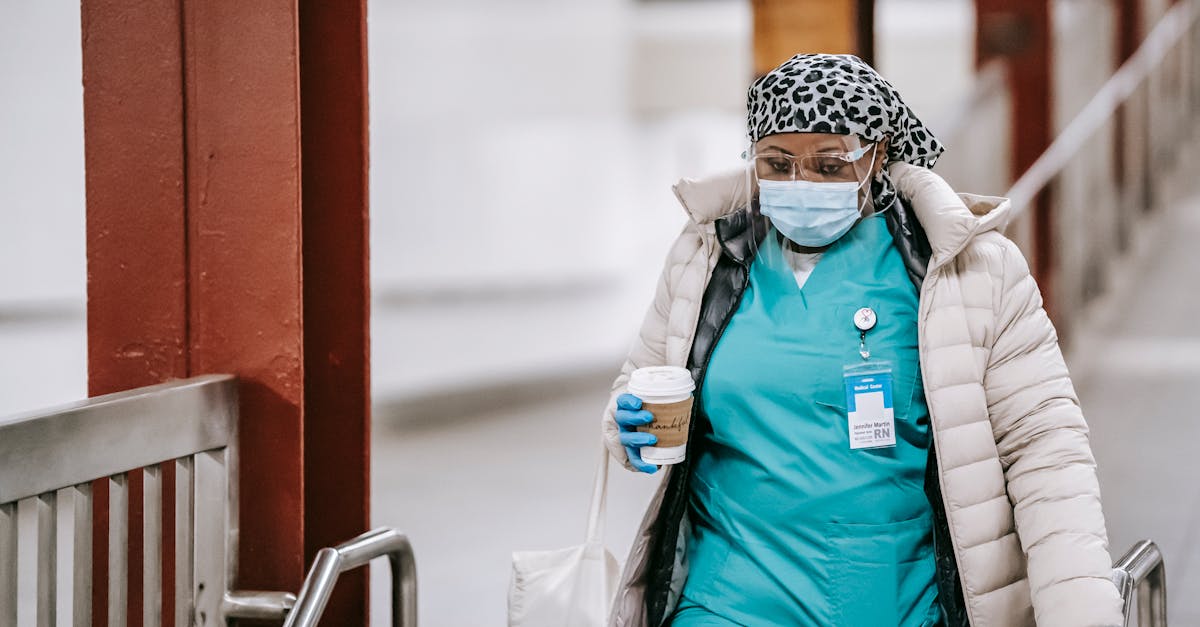 A healthcare worker in PPE and scrubs carrying a coffee cup, showcasing dedication during pandemic times.