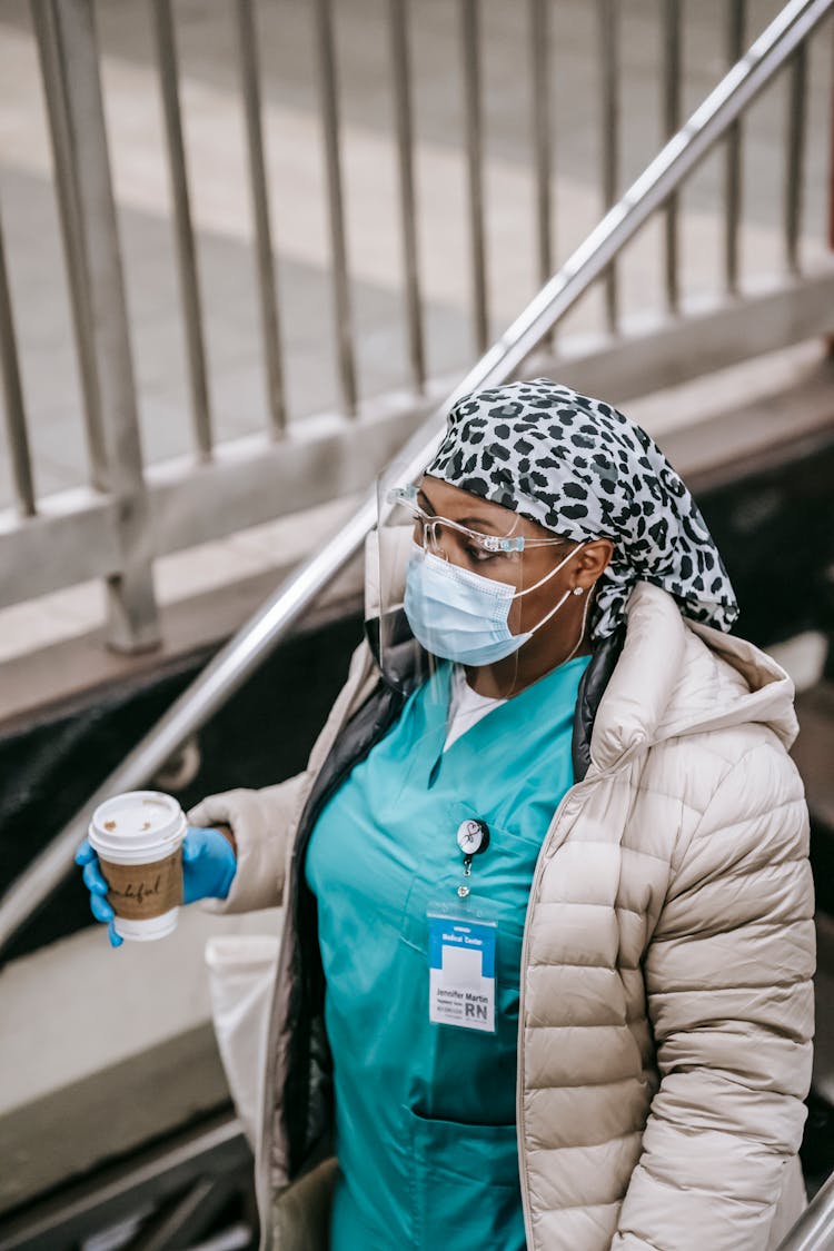 Black Female Nurse With Paper Cup Going Down To Underground Station