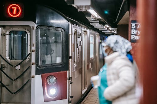 Unrecognisable female in medical uniform coat and with paper cup waiting for train arriving on subway platform