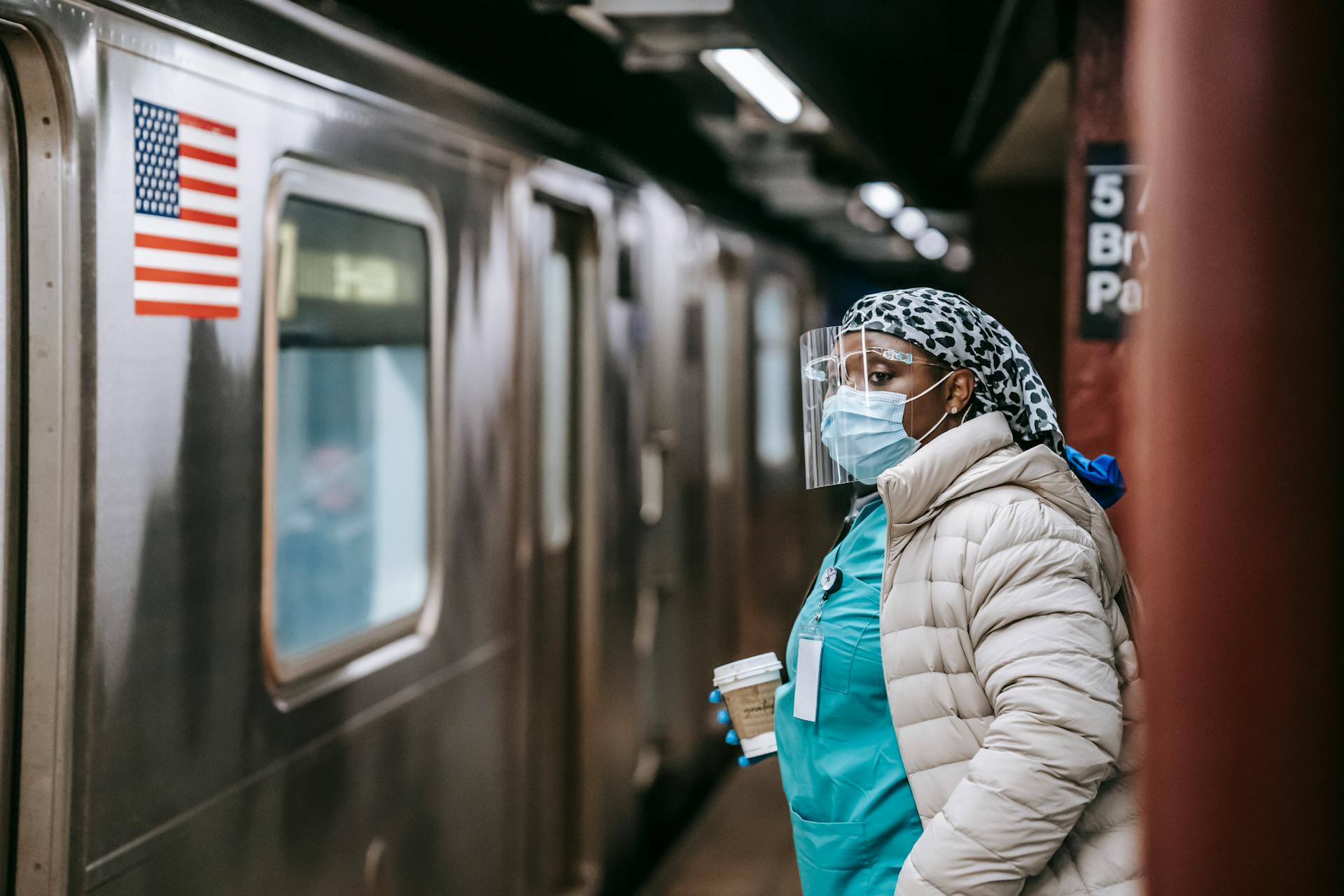 A healthcare worker in protective gear waits at a subway station amidst the COVID-19 pandemic.