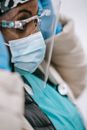 Crop black nurse in outerwear putting on face shield