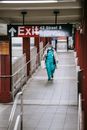 Full body African American female doctor in uniform and outerwear wearing protective mask and gloves walking in metro station passage