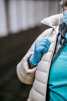 Close-up of a healthcare worker wearing gloves, a mask, and warm clothing indoors.