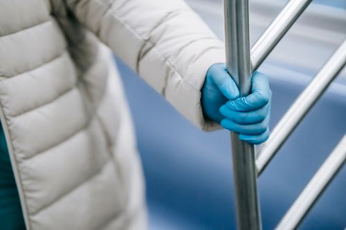 Free High angle crop anonymous passenger in warm clothes and latex gloves clasping handle while riding metro train during coronavirus epidemic Stock Photo