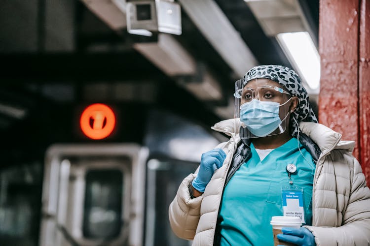 Pensive Black Nurse In Respirator Waiting For Train On Platform