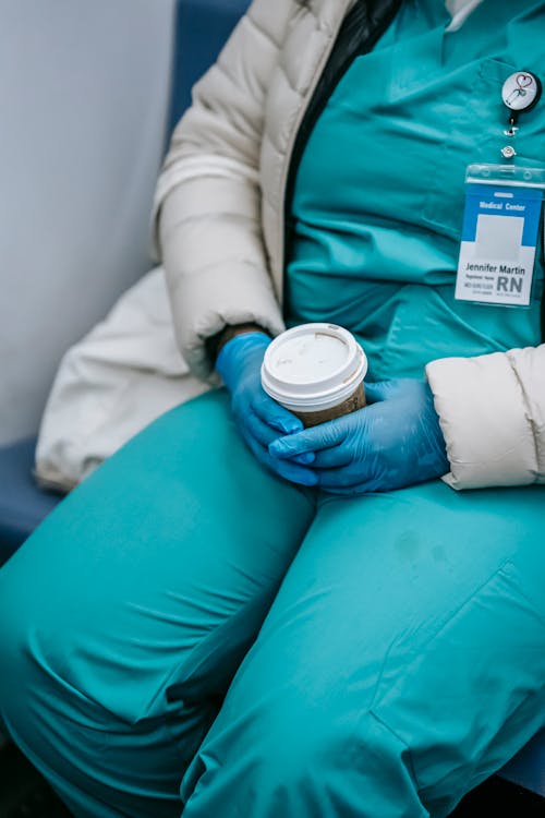 Crop unrecognizable nurse with takeaway coffee riding metro train