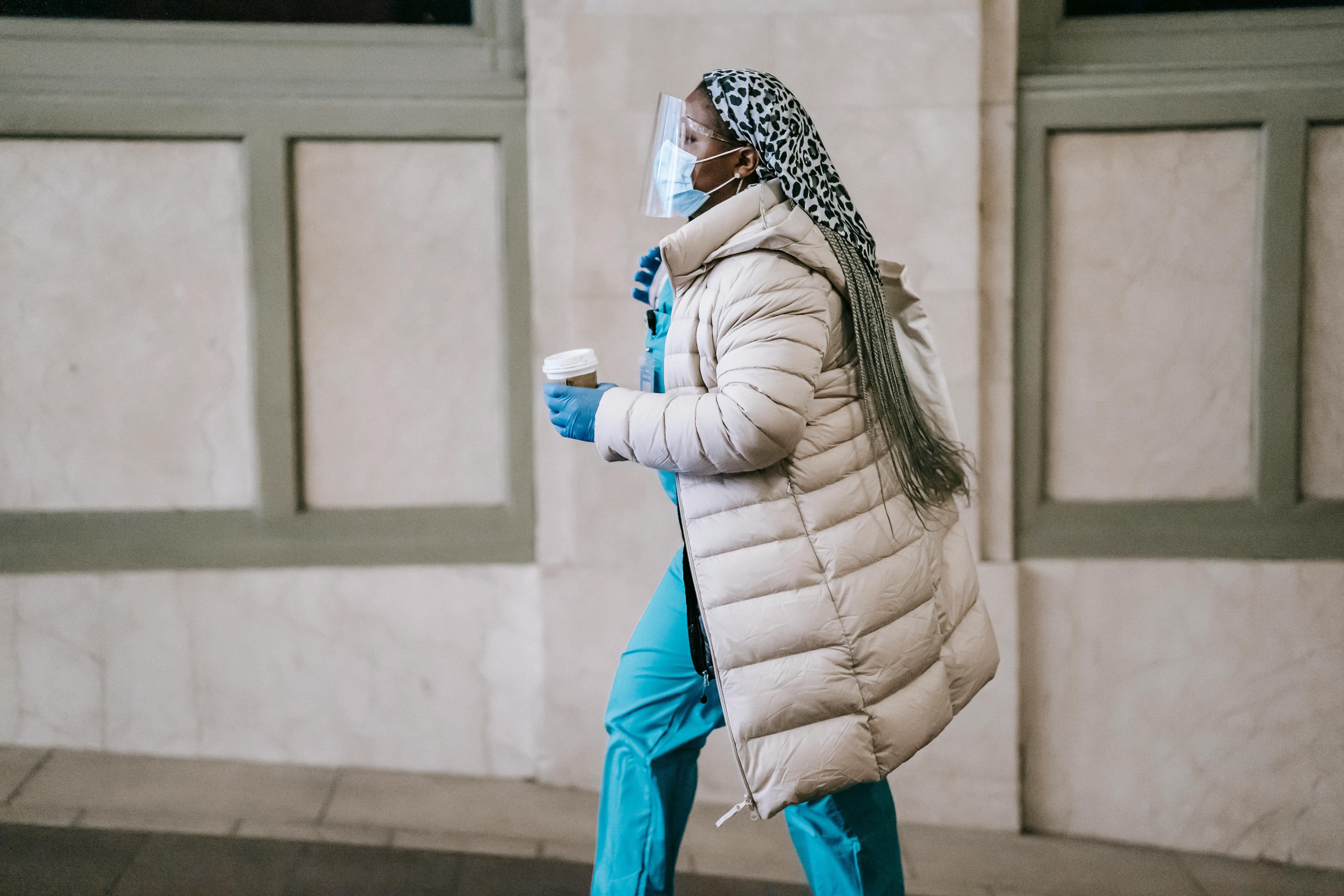 Black nurse in mask and outerwear using smartphone · Free Stock Photo