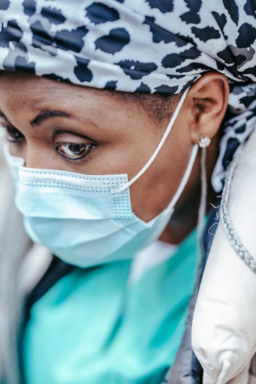 Crop focused mature ethnic female doctor in sterile mask and kerchief looking away during coronavirus pandemic