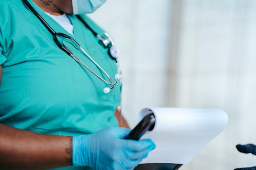 Free Side view of crop anonymous tattooed ethnic female medic in uniform with stethoscope and papers on clipboard Stock Photo