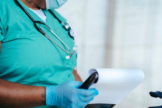 Side view of crop anonymous tattooed ethnic female medic in uniform with stethoscope and papers on clipboard
