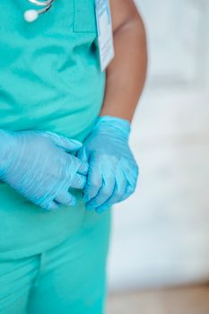 Crop anonymous ethnic female doctor in sterile gloves and green uniform with badge on blurred background