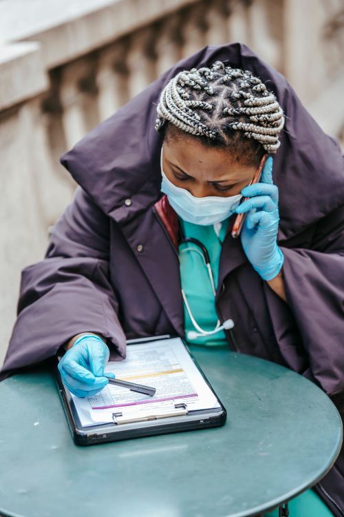 Free African American female doctor in uniform with document on clipboard speaking on cellphone in town Stock Photo