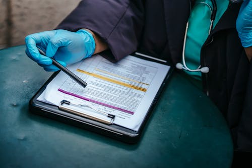From above of crop anonymous plump female doctor in disposable gloves working at table with paper on clipboard
