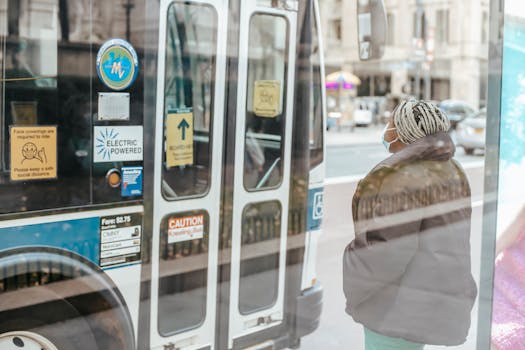 Photo by Laura James Through glass wall back view of anonymous ethnic female medic standing against public transport in town
