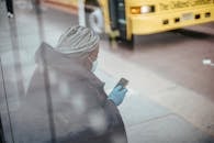 Through glass wall side view of African American female doctor using cellphone on pavement against bus on urban road