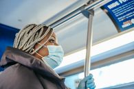 From below side view of African American female medic in disposable glove and mask looking forward in public vehicle